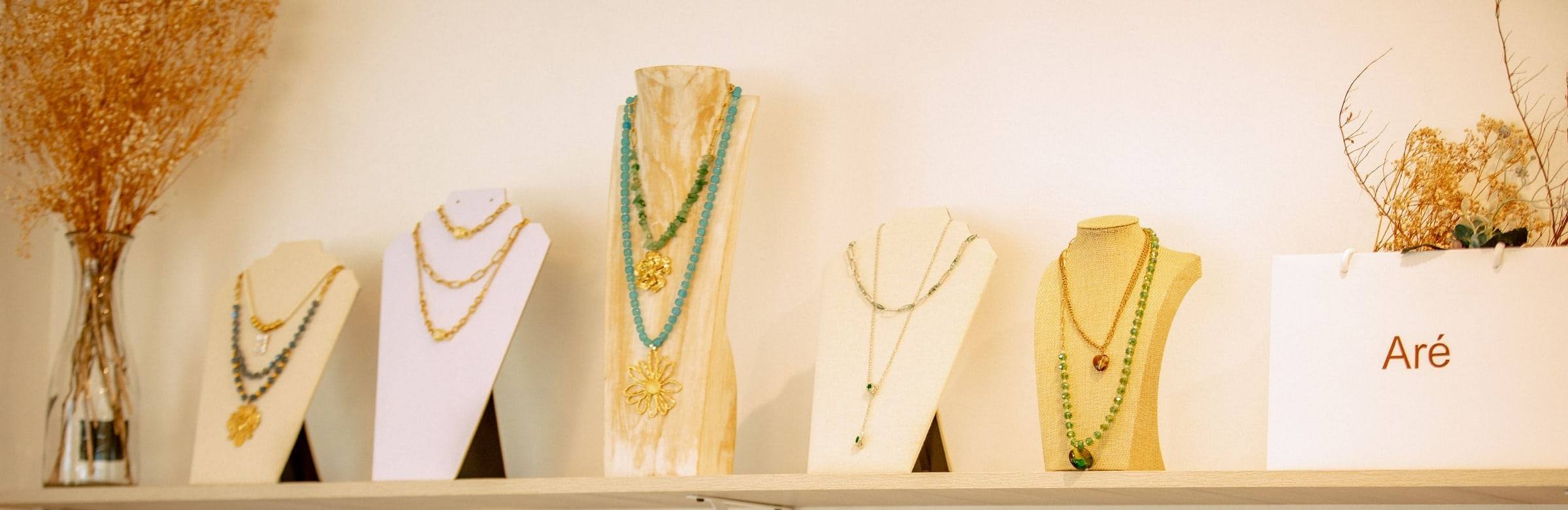Repisa de la tienda Aré con collares dorados y de piedras turquesa en bustos, junto a la bolsa con el logo de Aré