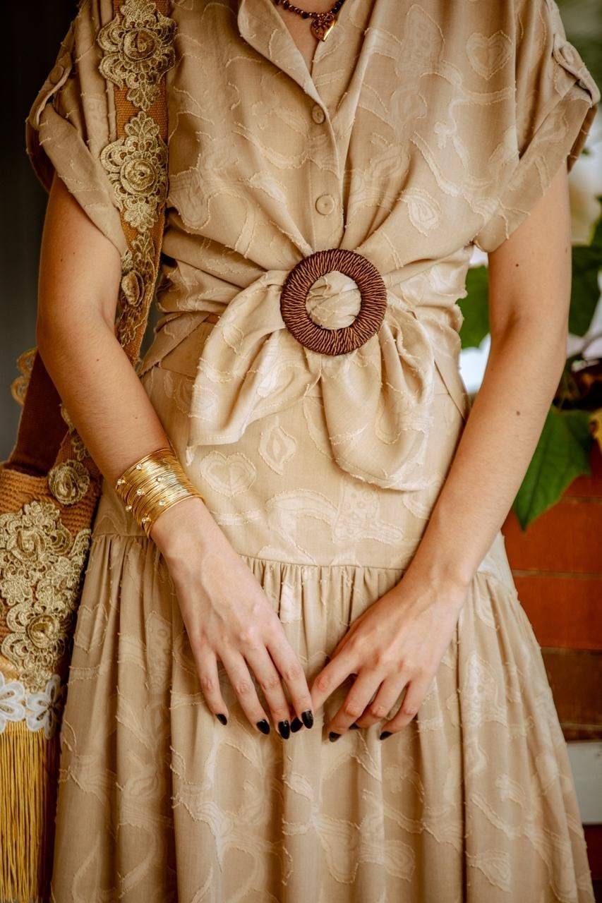 Brazalete dorado y cinturón tejido sobre un vestido de lino