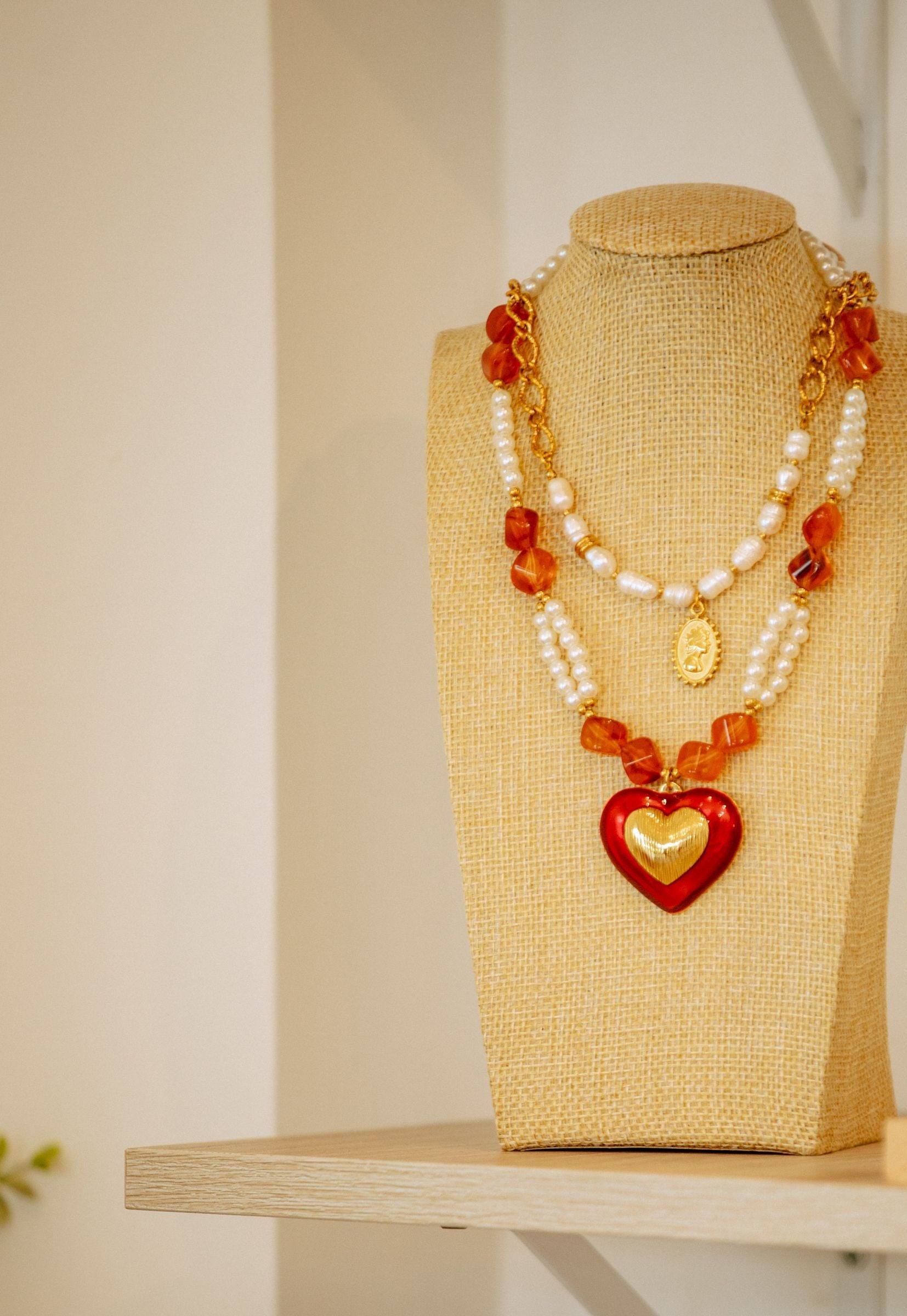 Collar de perlas con corazón rojo en un busto de lino